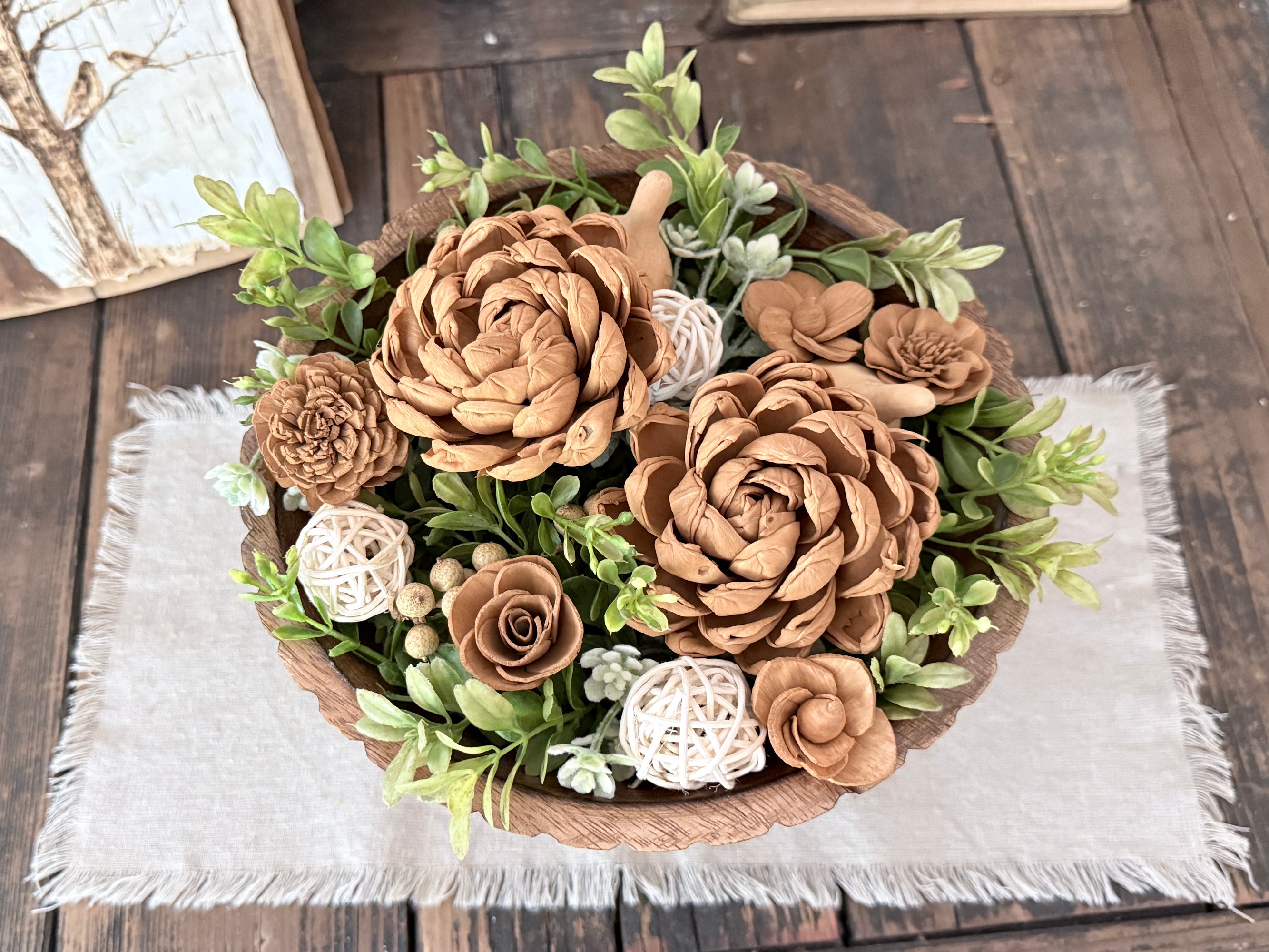 Decorative teak wood bowl with brown and white wood flowers on a wooden surface