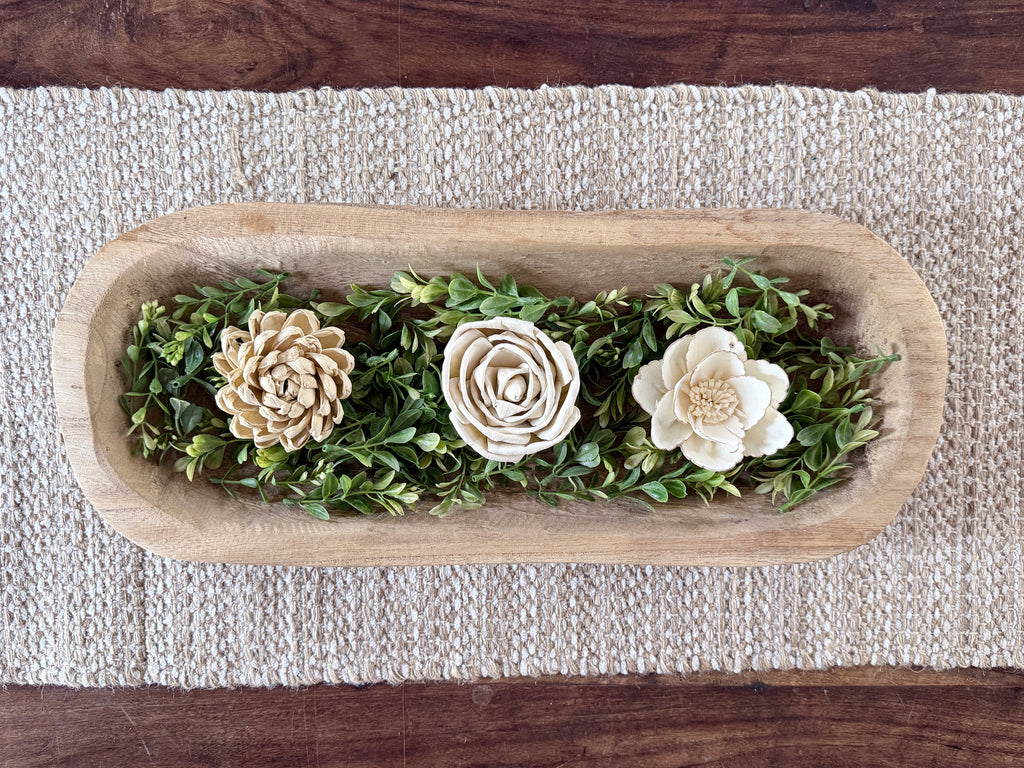 Decorative wooden tray with artificial wood flowers  laid on boxwood greenery on a coffee table.