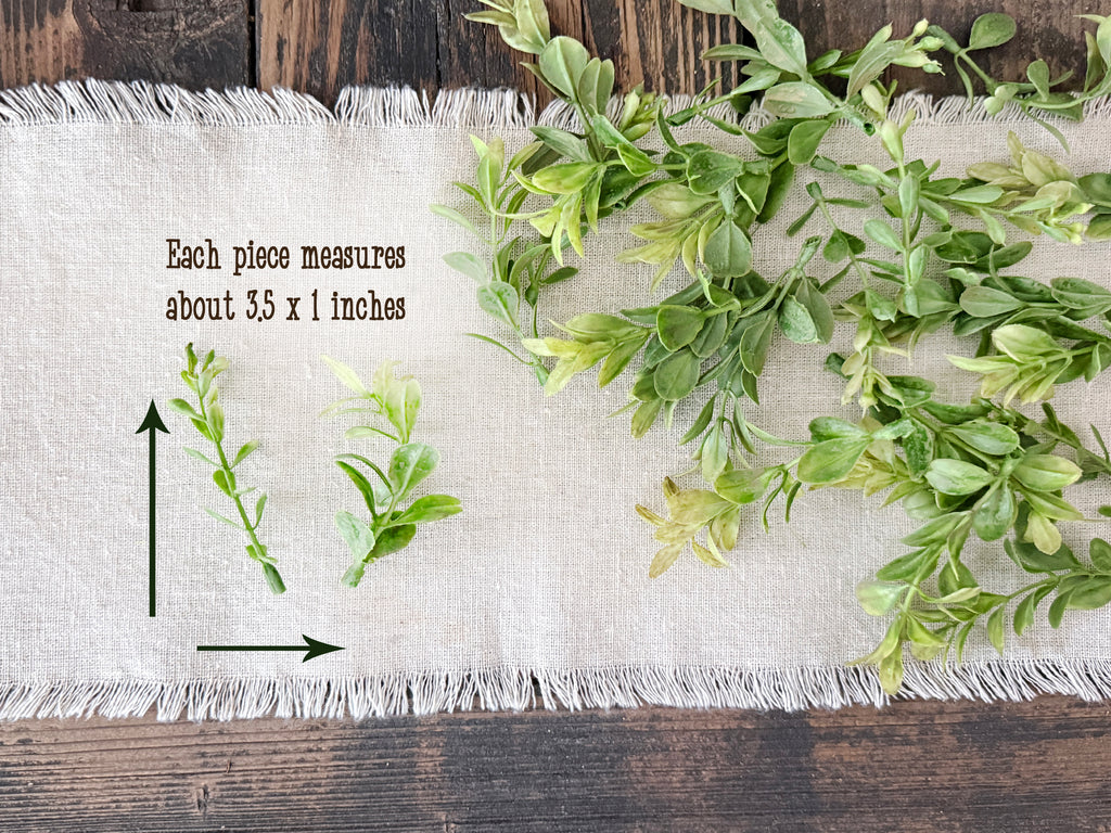 Green leafy branches on a white fabric with measurements and text on a wooden surface
