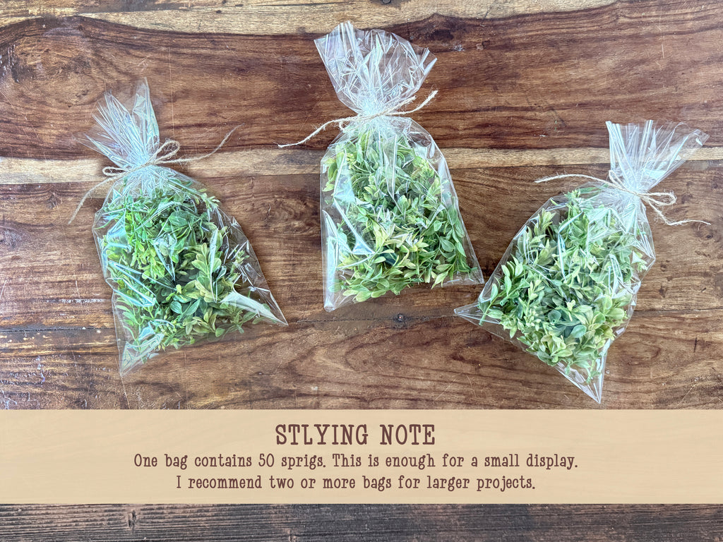 Three bags of faux greenery on a wooden surface with text below.