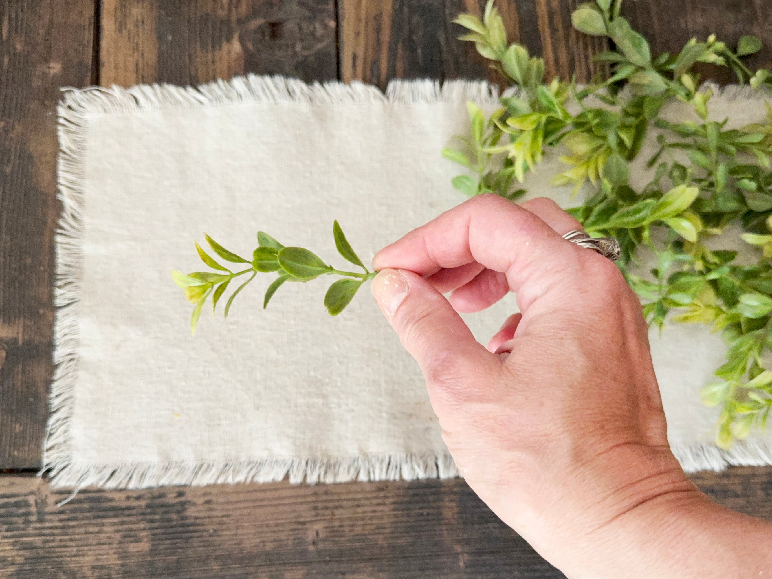 Hand placing a green leaf on a white fabric mat with a wooden background