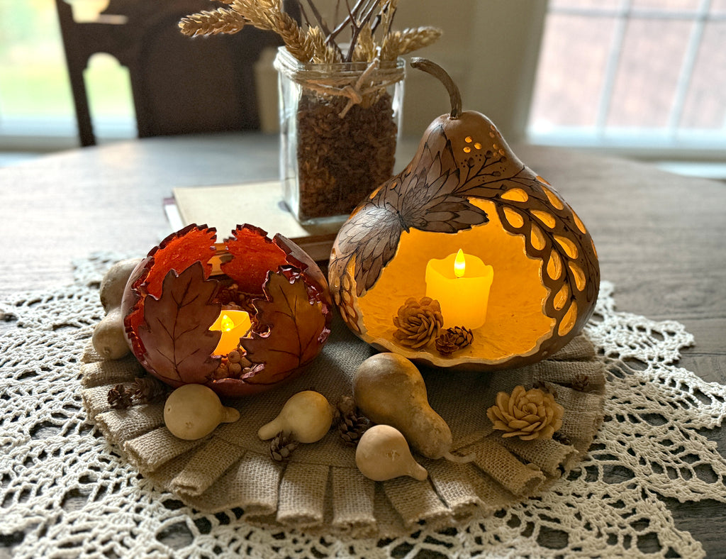Two carved gourd lit with candles on rustic table.