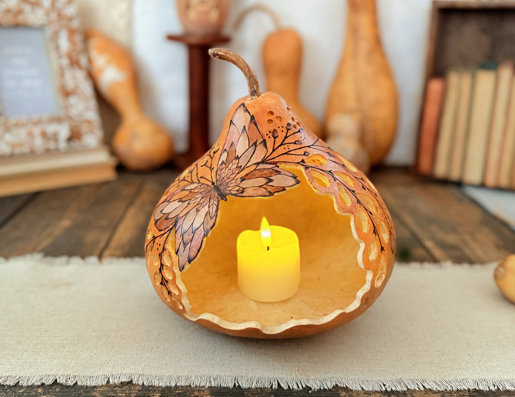 Carved butterfly gourd with lit candle inside. Antique books and dried gourds sit in the background