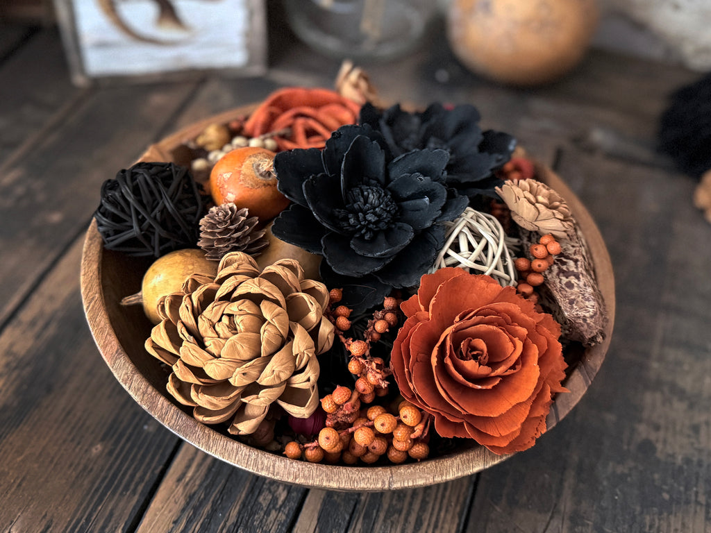 Decorative bowl with autumn-themed flowers and pinecones on a wooden surface