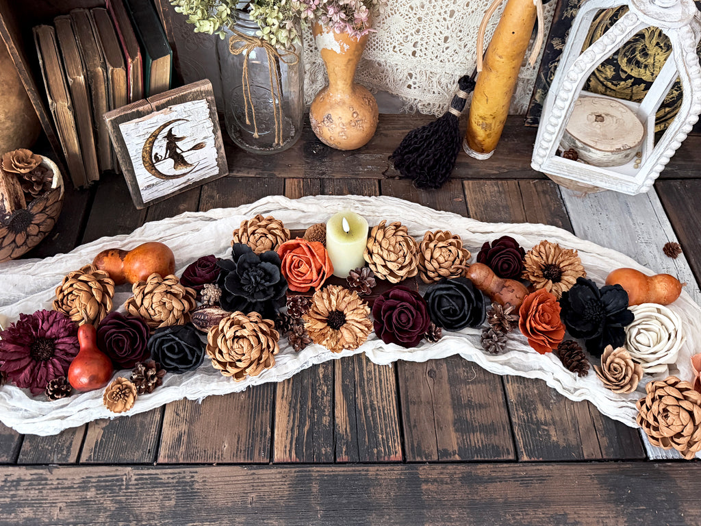 Decorative table runner arrangement of flowers and gourds on a wooden table with lanterns and candles.