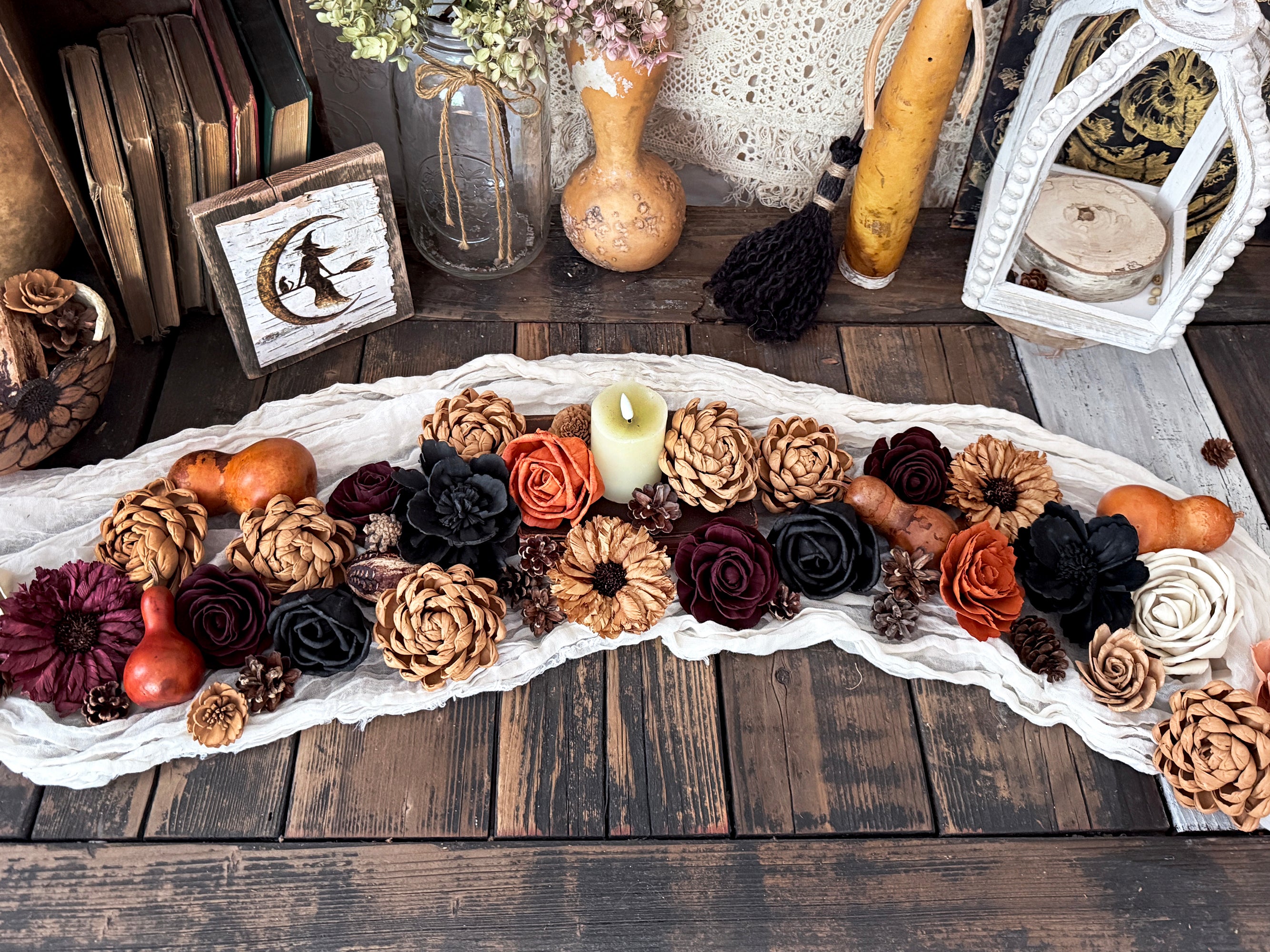 Decorative table runner arrangement of flowers and gourds on a wooden table with lanterns and candles.