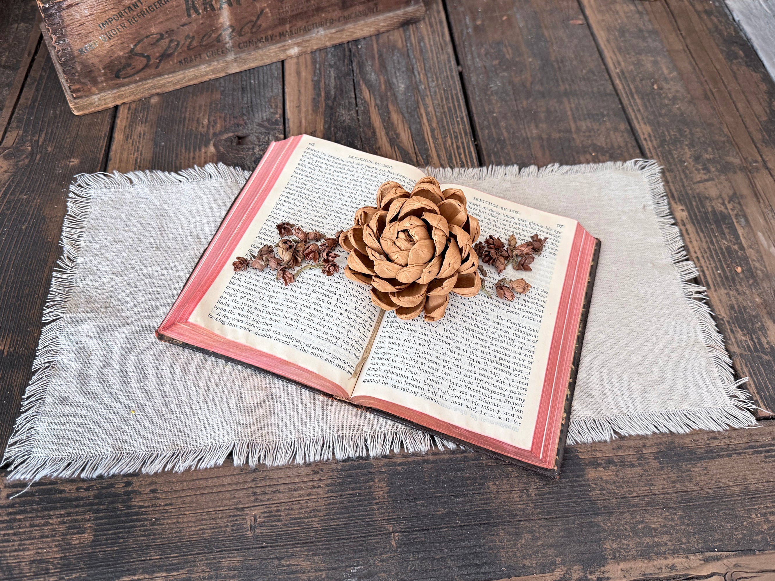 Open book with a decorative wood flowers and cedar cones scattered on a wooden surface