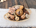 Decorative cat gourd is nestled in with smaller pet themed gourds, woods flowers, dried botanicals and twig ball in a ceramic bowl with handles. 