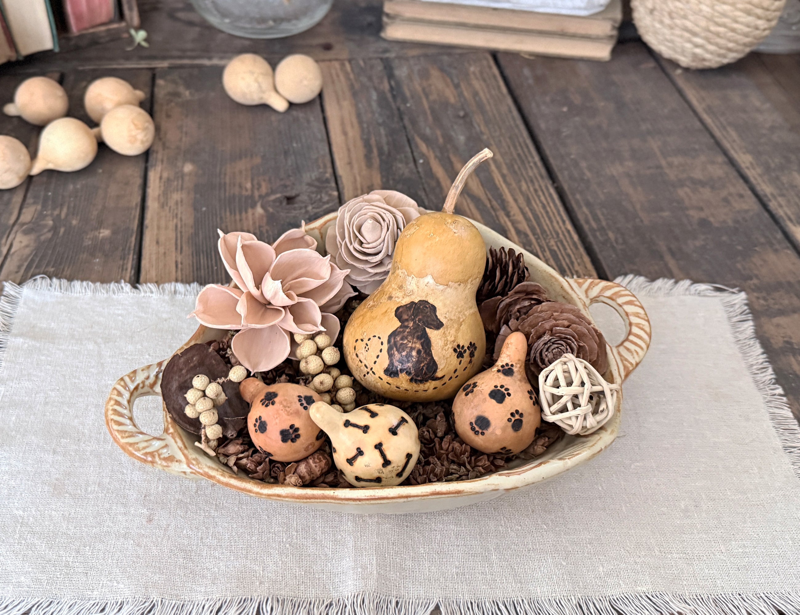 Decorative bowl arrangement of a Dachshund gourd and flowers in a ceramic bowl on a wooden table.