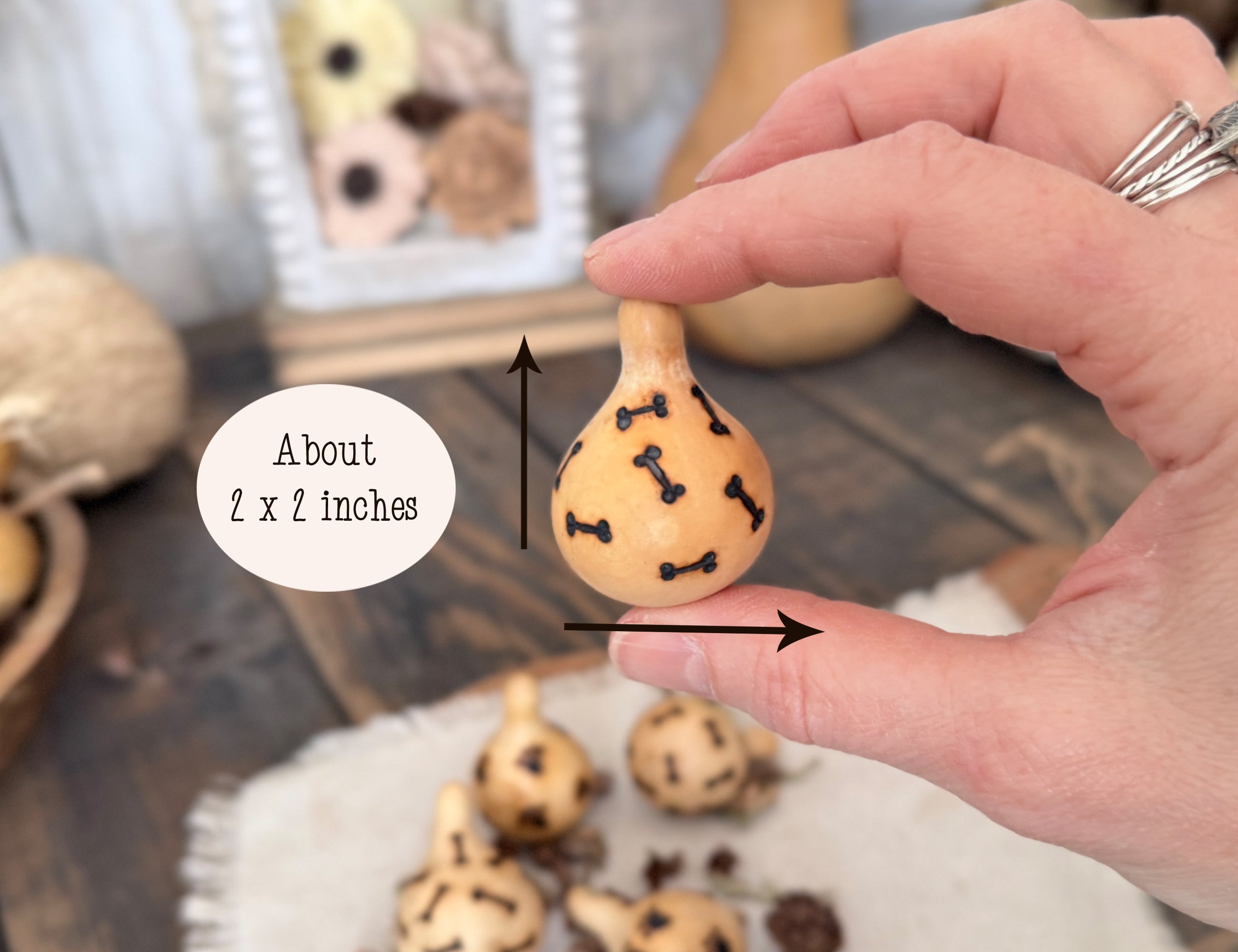 Hand holding a small gourd with burned patterns of dog bones, labeled 'About 2 x 2 inches'.