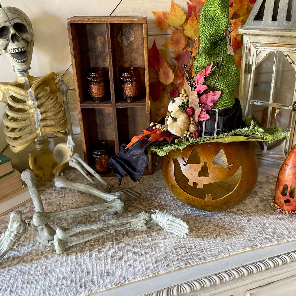 A fall table scape with carved gourd characters, a skeleton and a lantern.