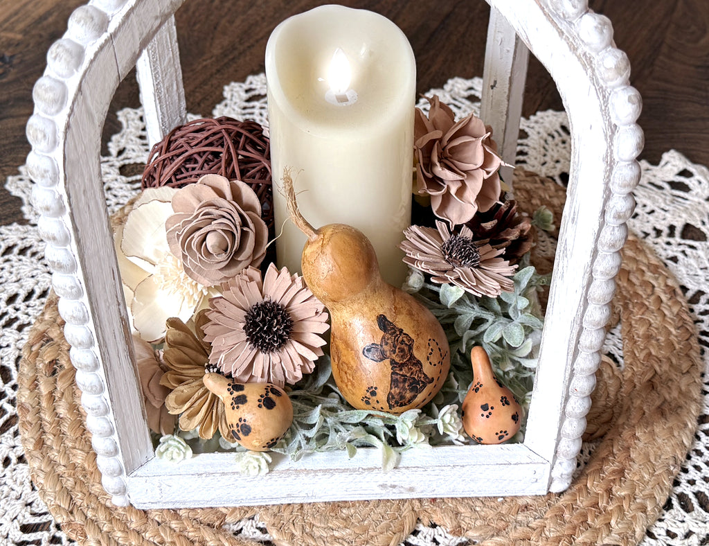Decorative lantern with candle, flowers, and gourds on a doily