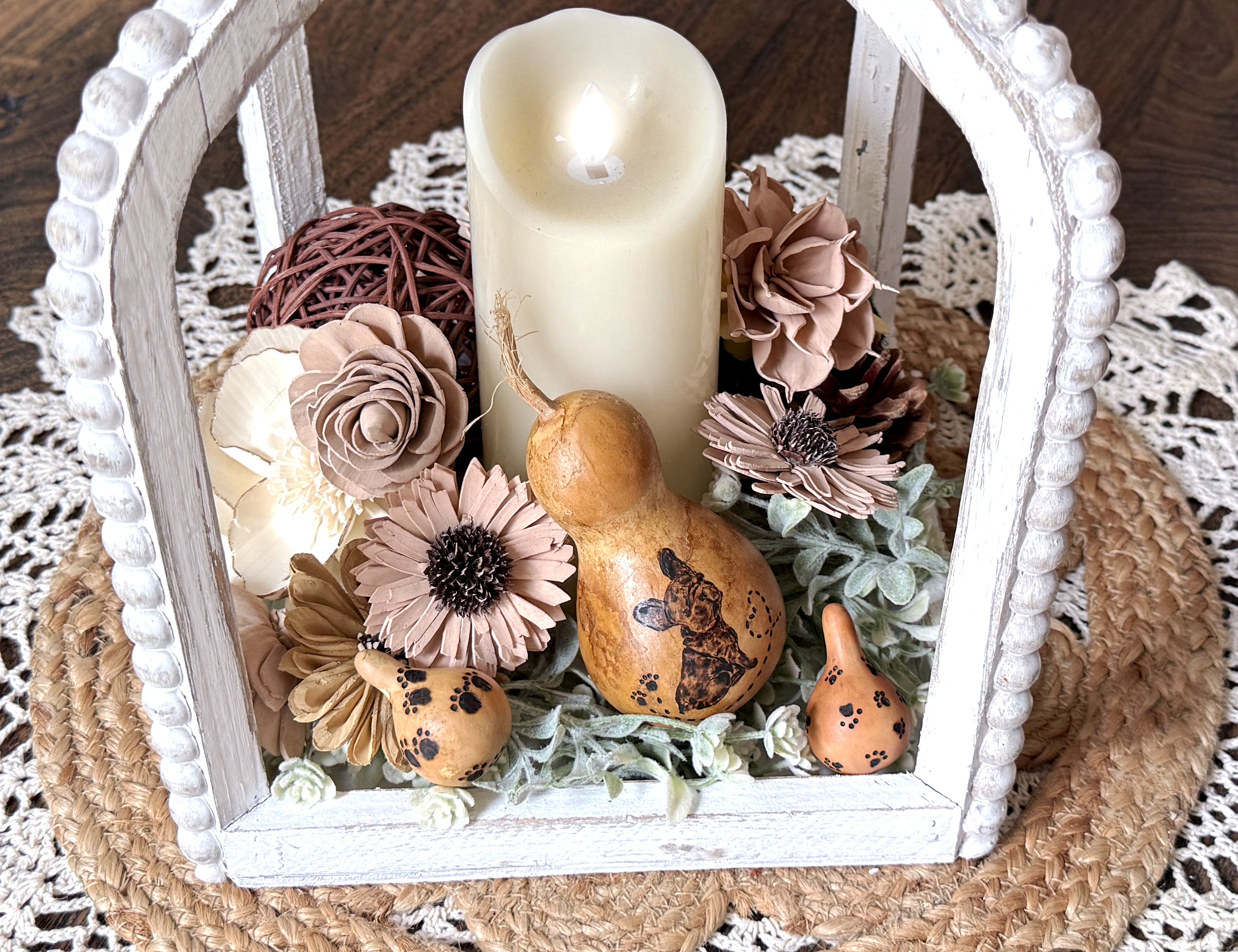 Decorative lantern with candle, flowers, and gourds on a doily