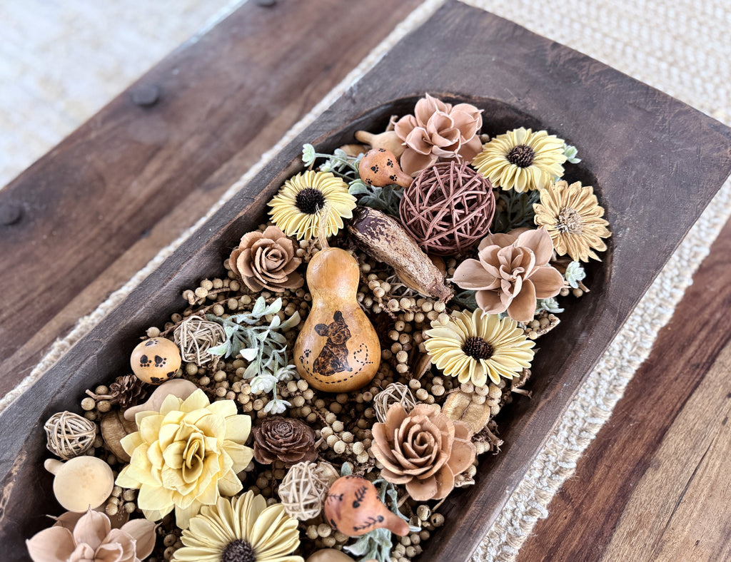 Decorative dough bowl arrangement of flowers and gourds on a coffee table