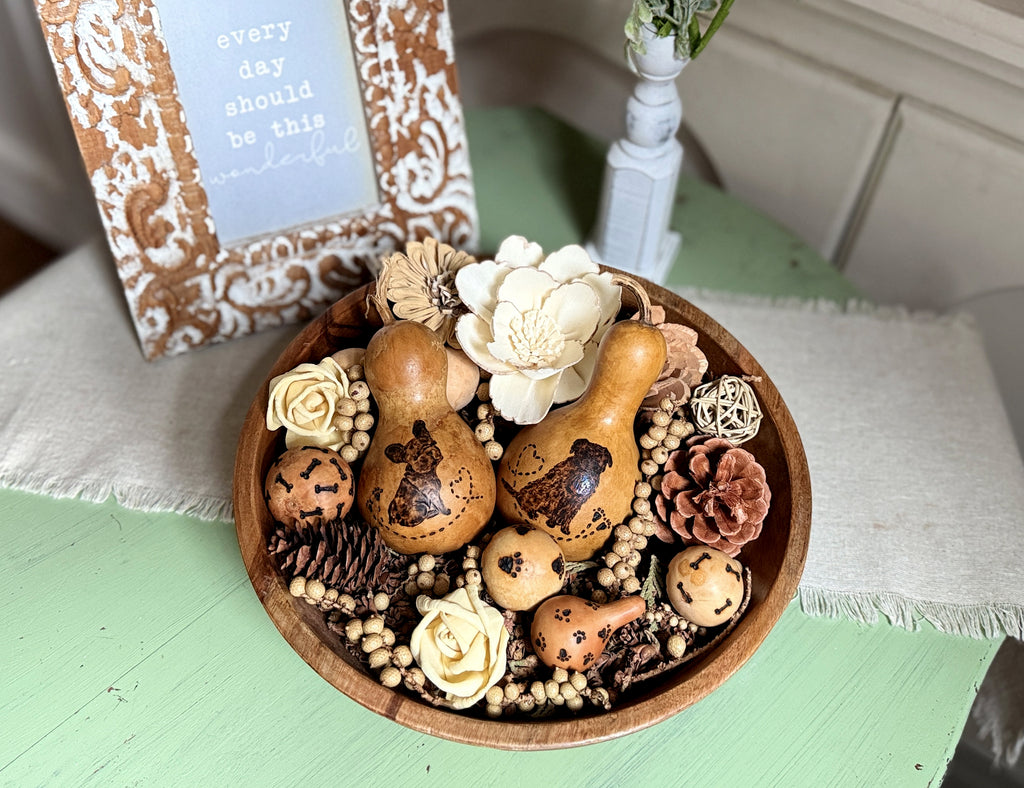 Decorative bowl with doggy gourds, flowers, and pinecones on a green surface.