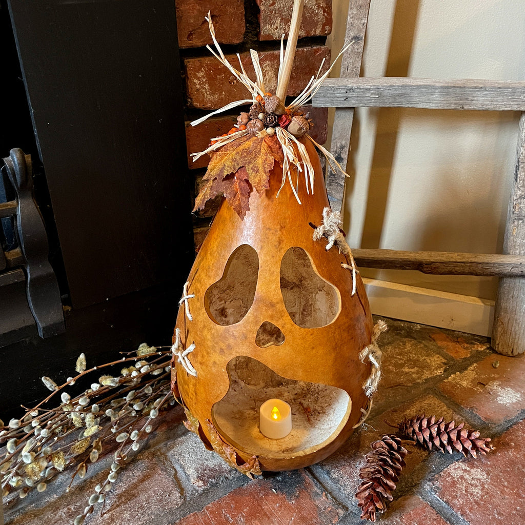 Decorative gourd with cut-out shapes and a candle on a stone surface.
