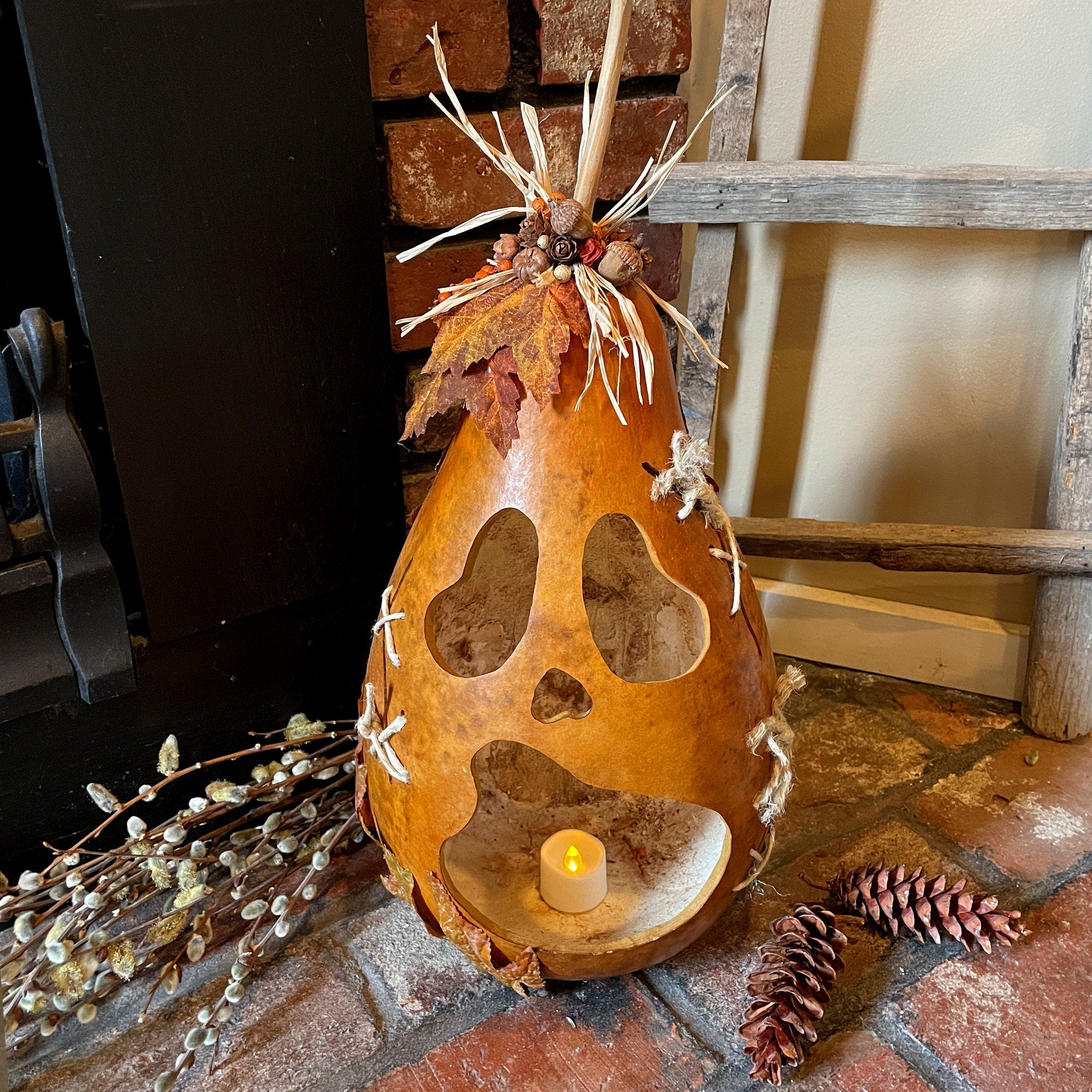 Decorative gourd with cut-out shapes and a candle on a stone surface.