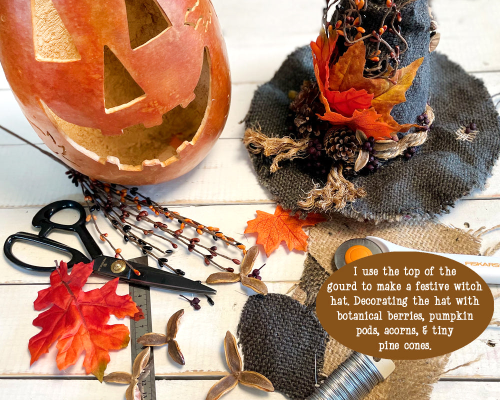 Decorative witch hat with autumn elements and a pumpkin on a wooden surface.