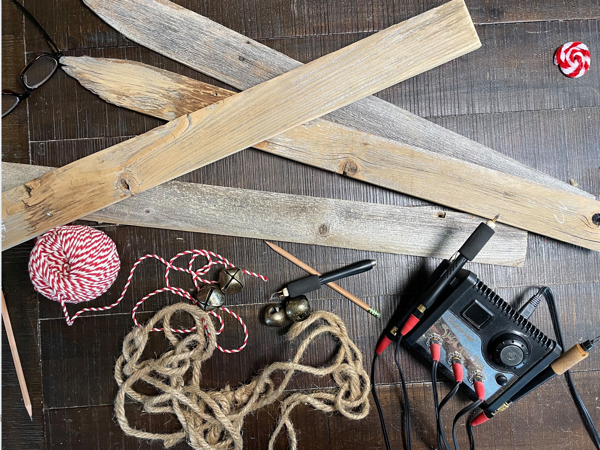 Wooden planks, yarn, tools, and a hot glue gun on a wooden surface.