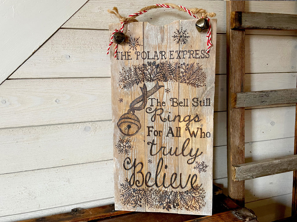 Wooden sign with Christmas-themed text and graphics on a wooden surface.