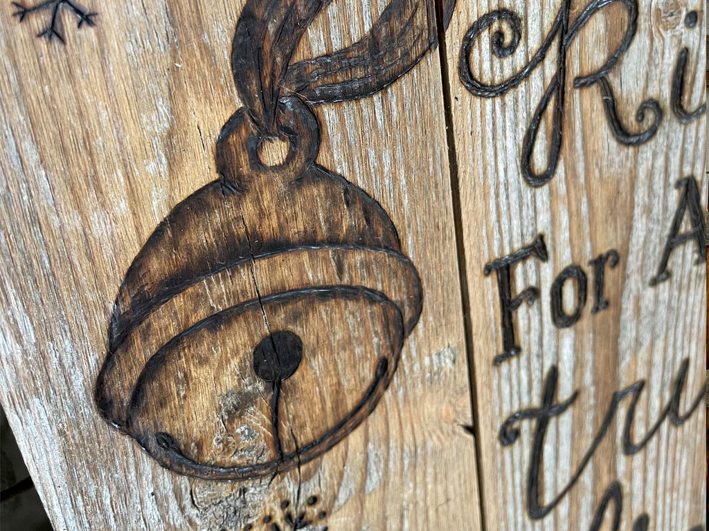 Wooden ornament with bell design and engraved text on a rustic wooden background