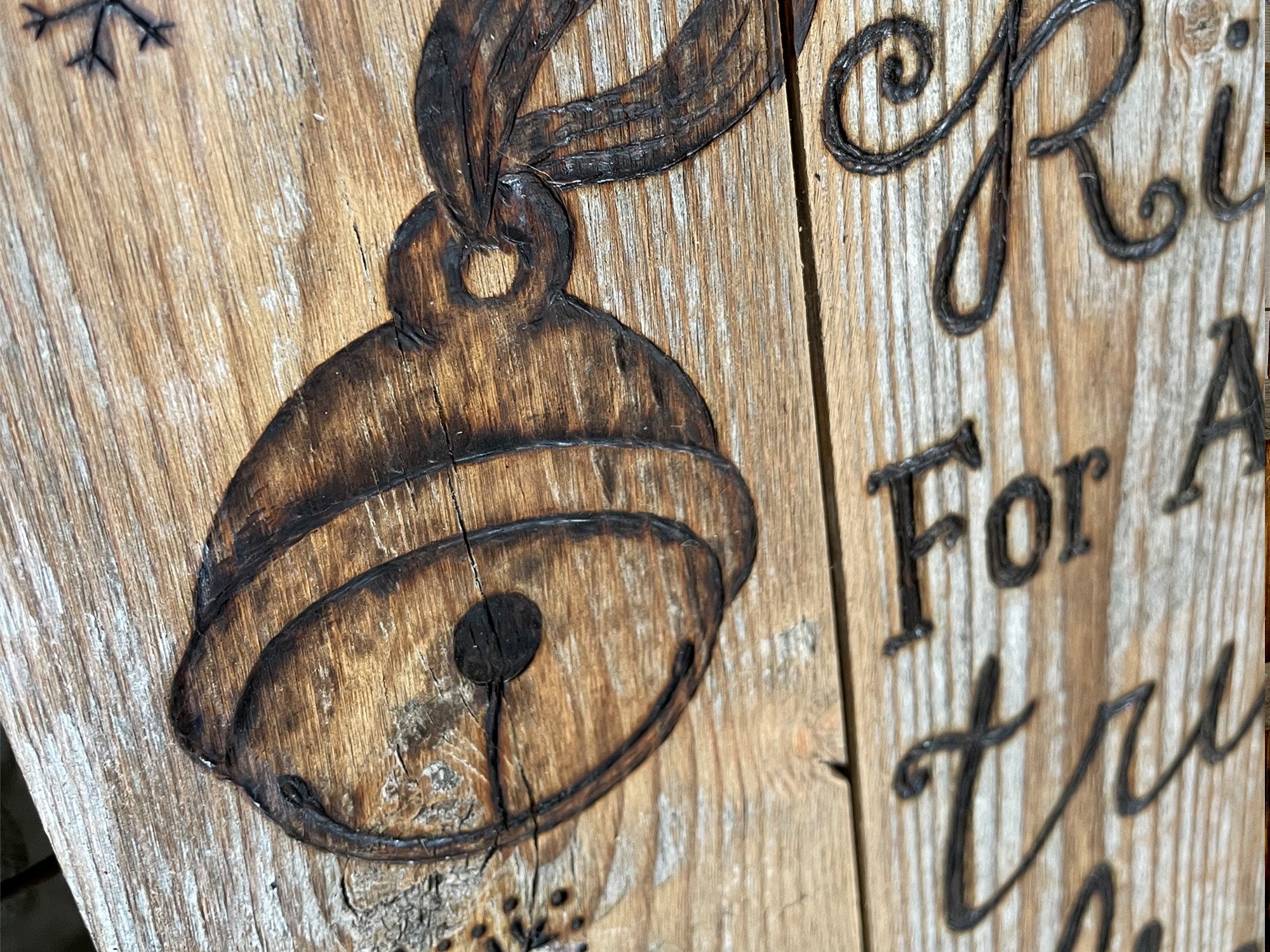 Wooden ornament with bell design and engraved text on a rustic wooden background