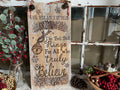 Wooden sign with Christmas-themed text and decorations in a rustic setting.