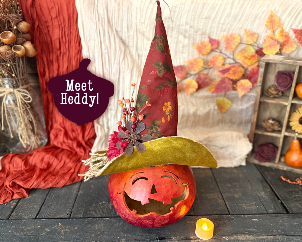 Decorative pumpkin with a hat labeled 'Meet Heddy' in an autumn-themed setting.