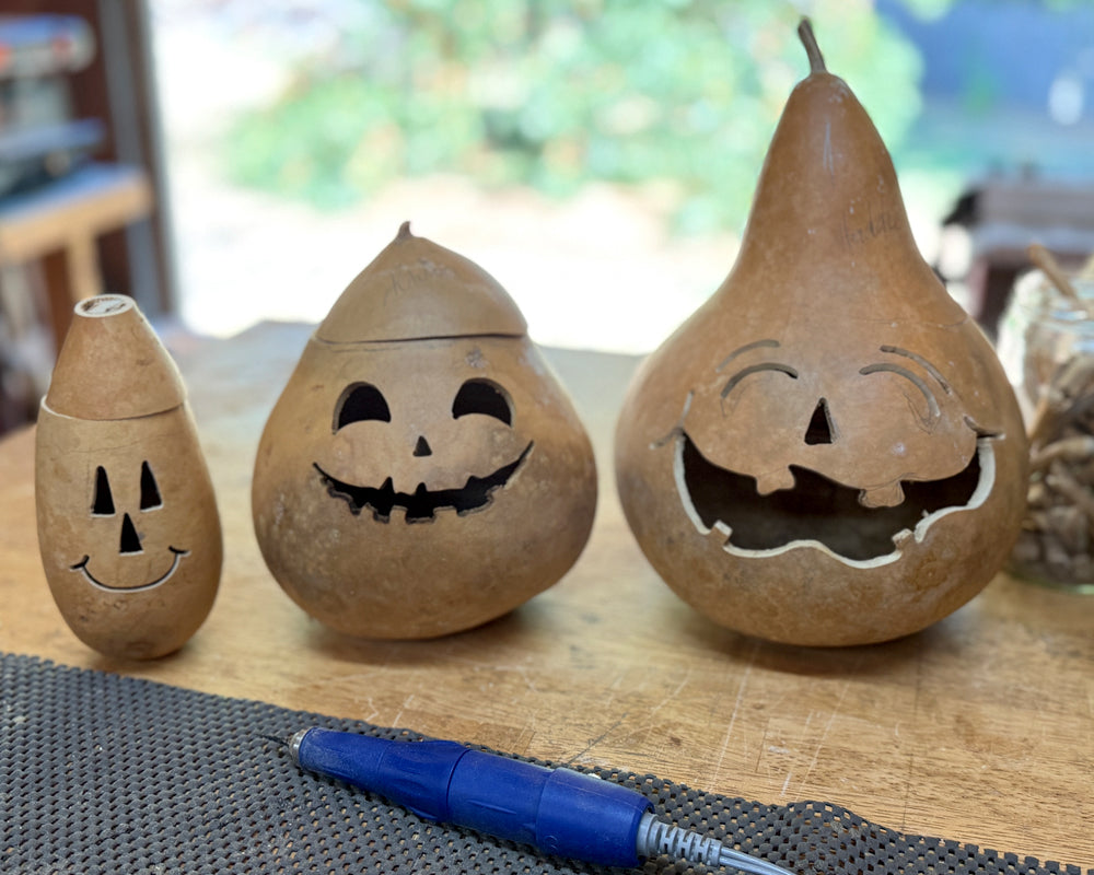 Three gourd pumpkins with carved faces on a wooden surface.