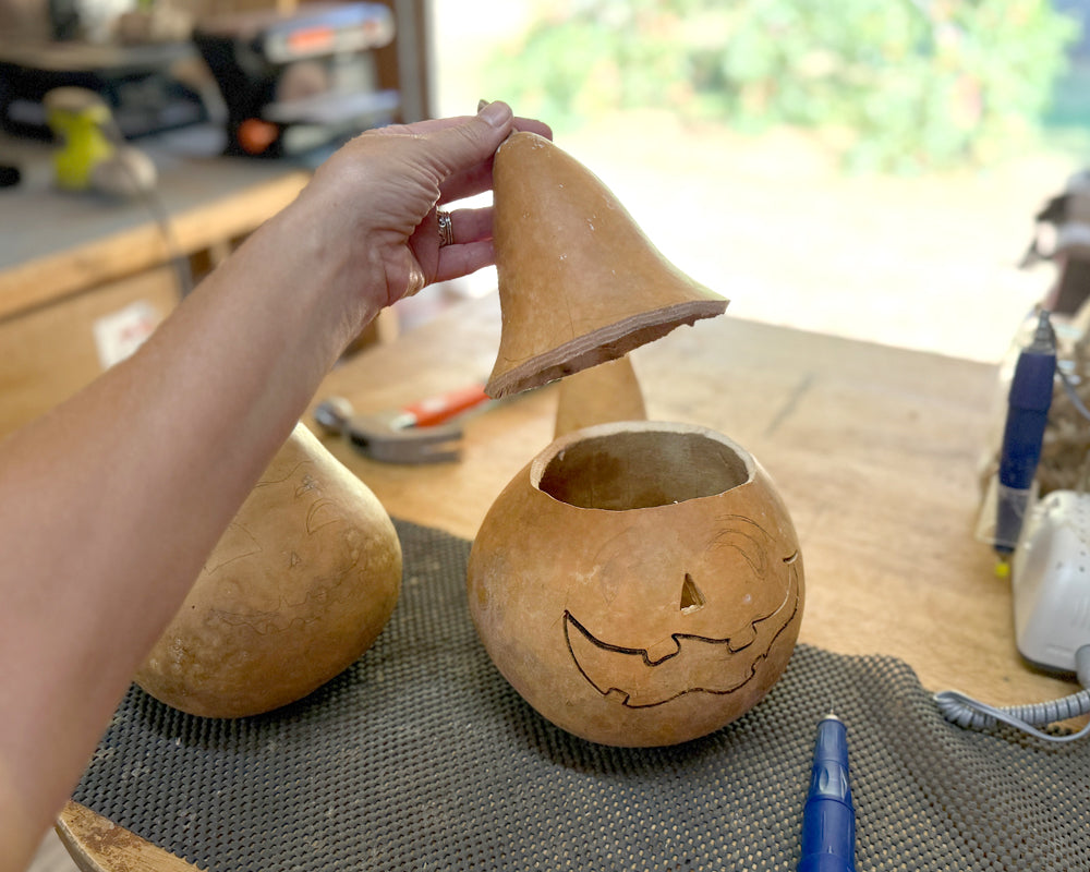 Person carving a pumpkin into a jack-o'-lantern with a cone-shaped tool on a table.