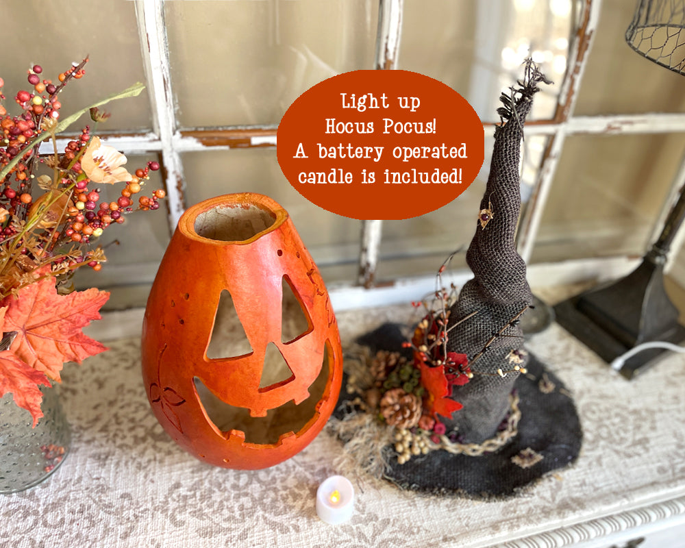 Halloween-themed decor with a jack-o'-lantern candle holder and witch hat on a table.