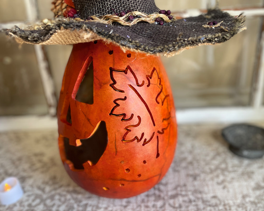 Decorative pumpkin with leaf design and black hat on a textured surface.