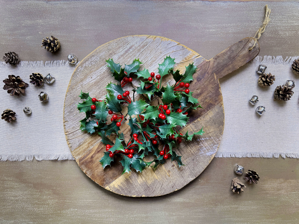A vintage bread board holds a display of sprinkled holly berries. 