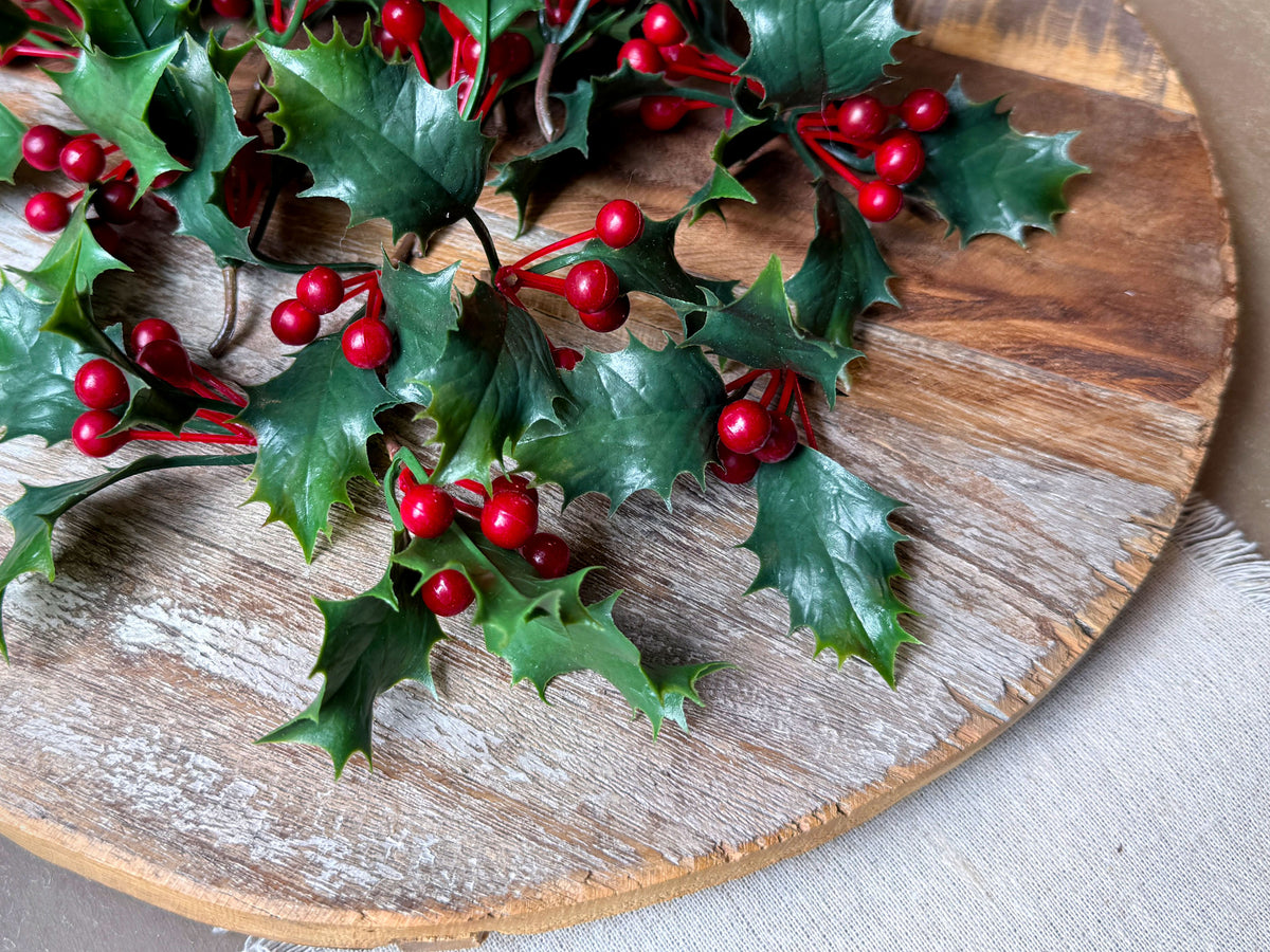 A closeup image of real touch holly berry leaves and berries on a wood board