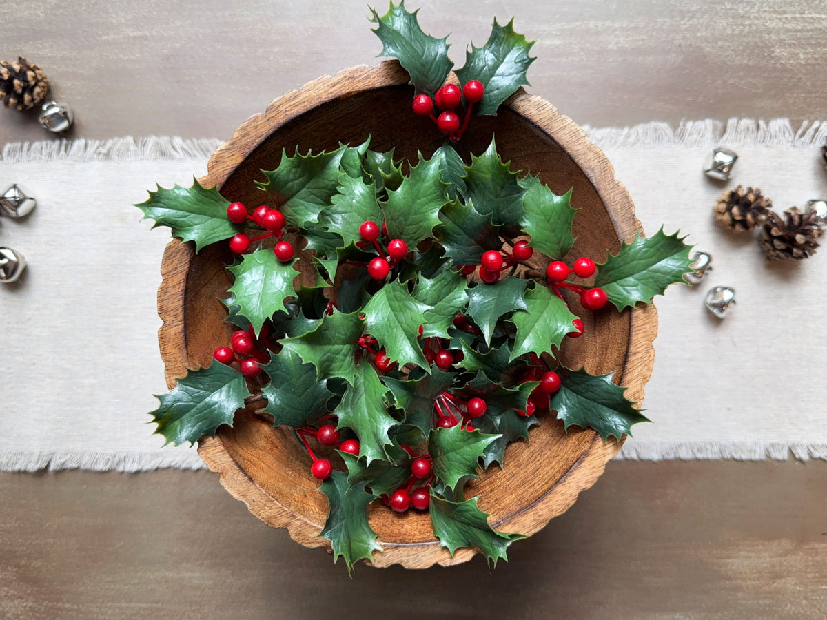 A top down image of round wood bowl with a  display of sprinkled holly berries. 