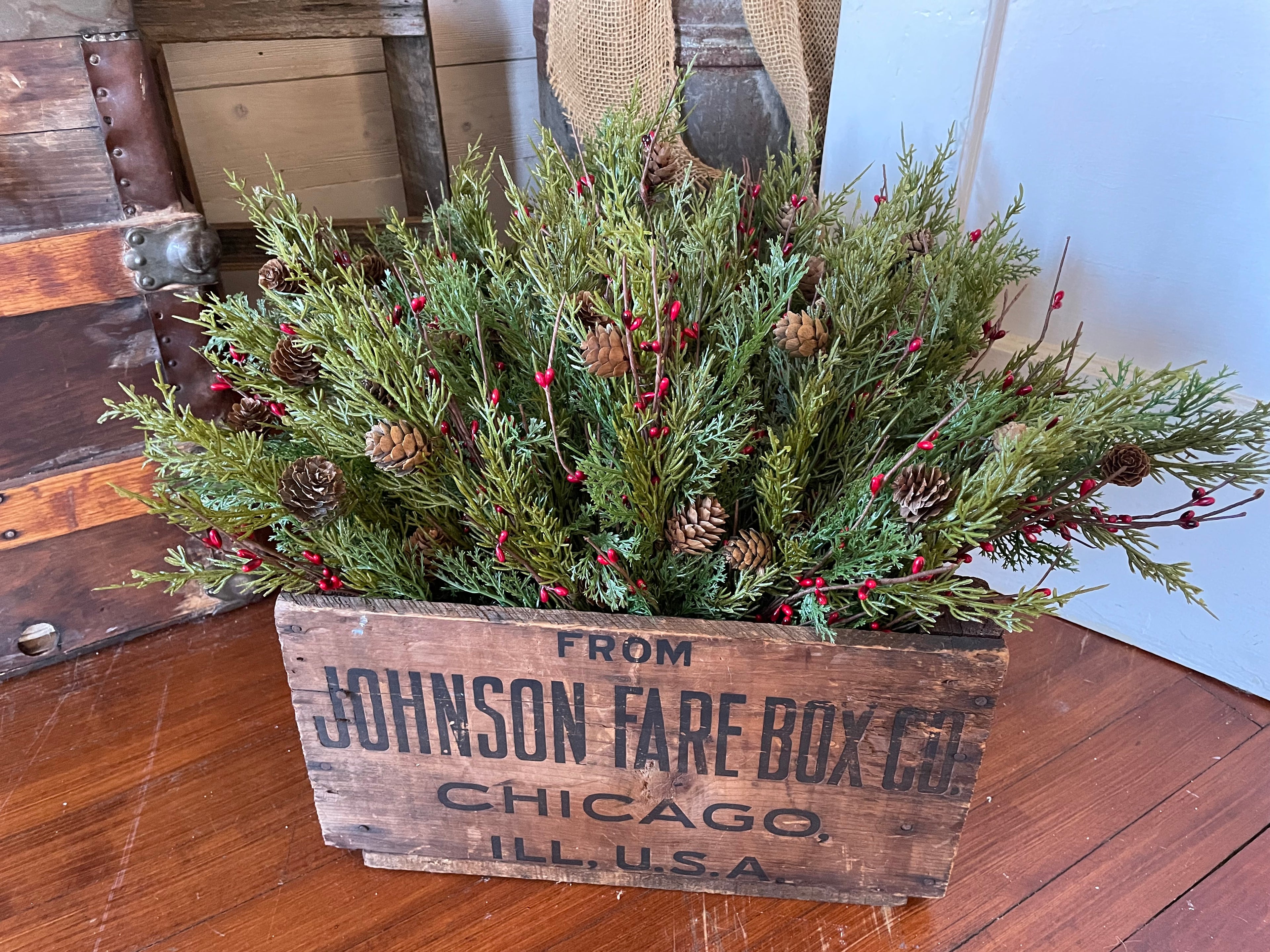 Decorative arrangement of greenery and pinecones in a vintage wooden box on a wooden floor.