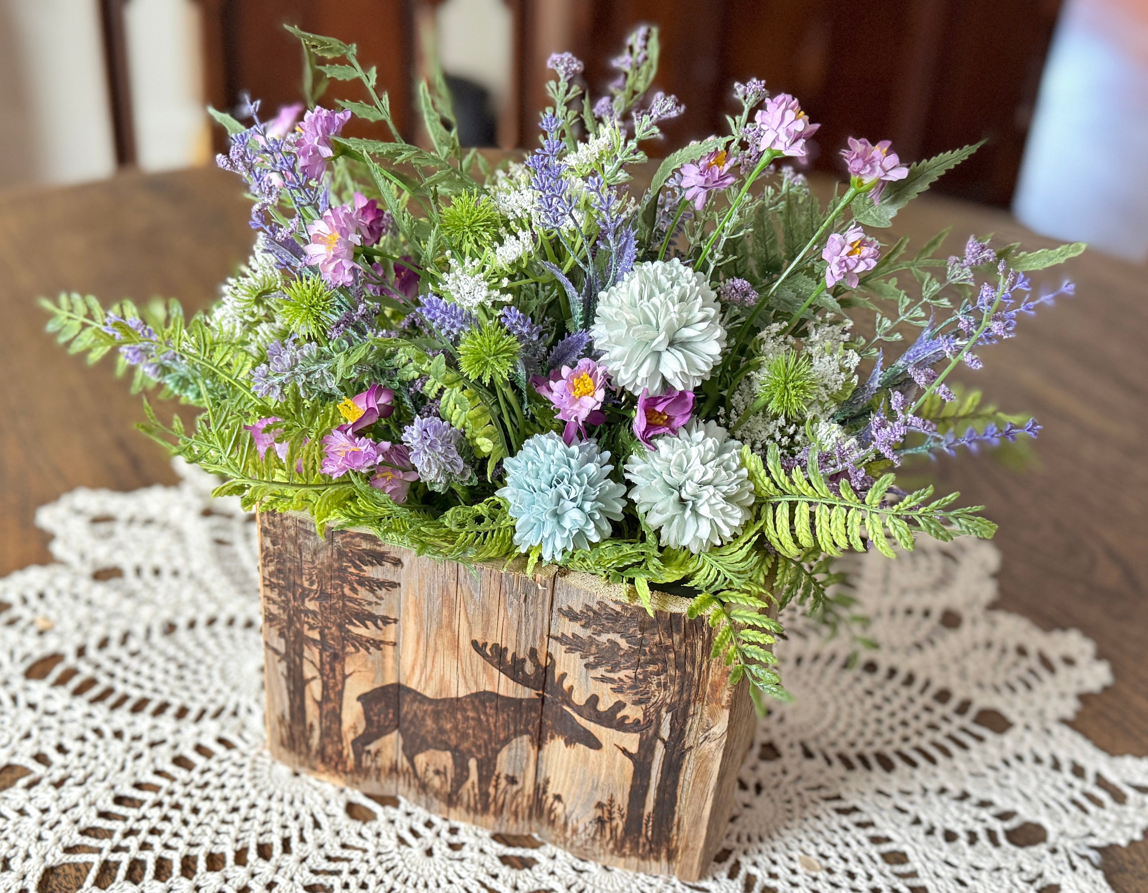 Floral arrangement in a wooden box with moose design on a lace doily