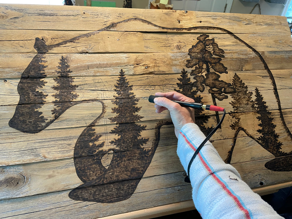 Hand holding a carving tool over a wooden surface with engraved patterns