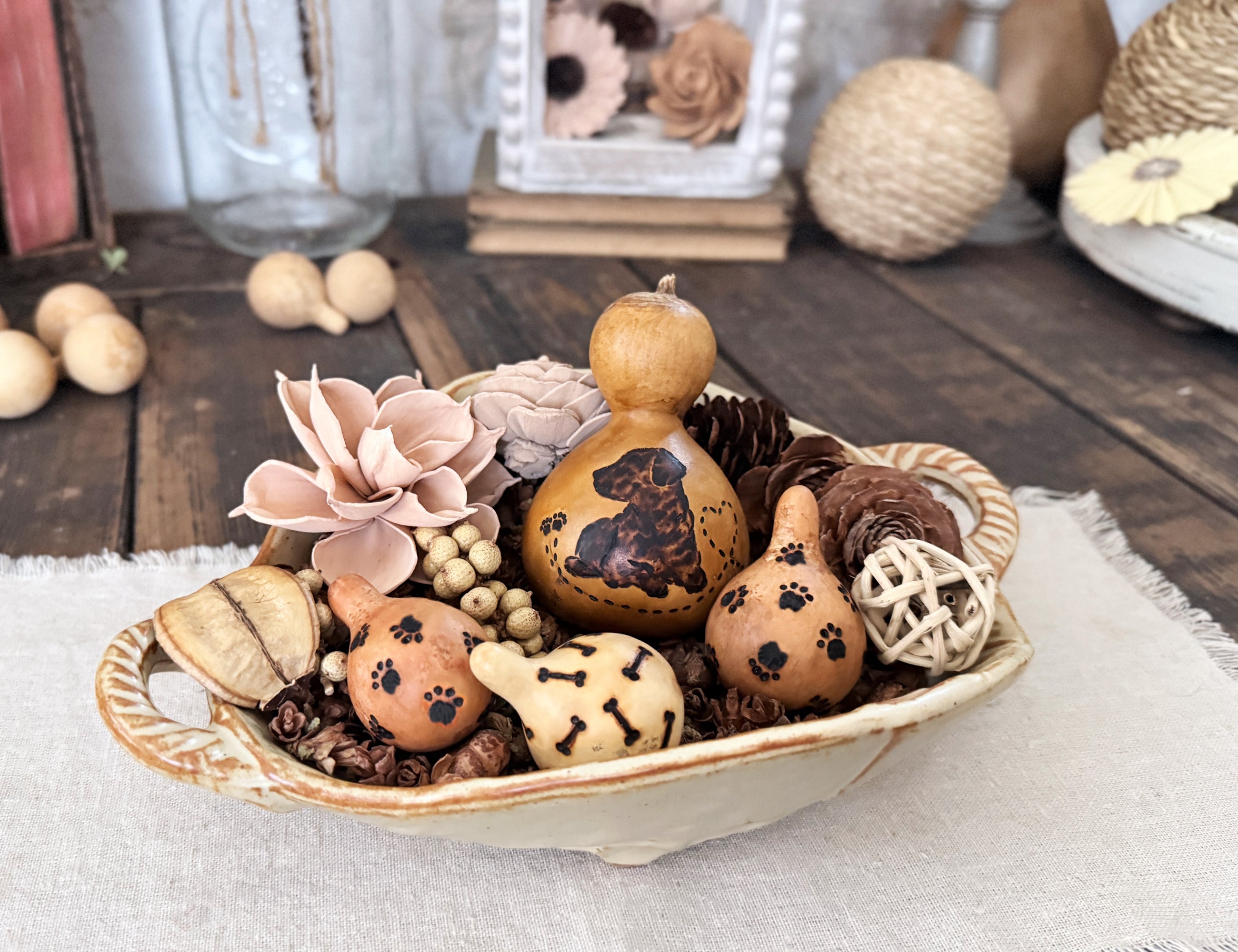 Decorative bowl with dog themed gourds, flowers, and pinecones on a wooden surface