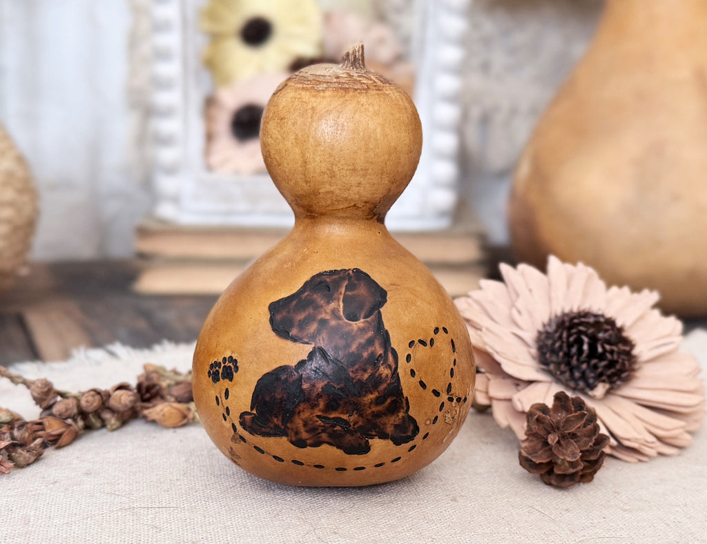 Decorative gourd with a dog design on a table with flowers and pinecones.