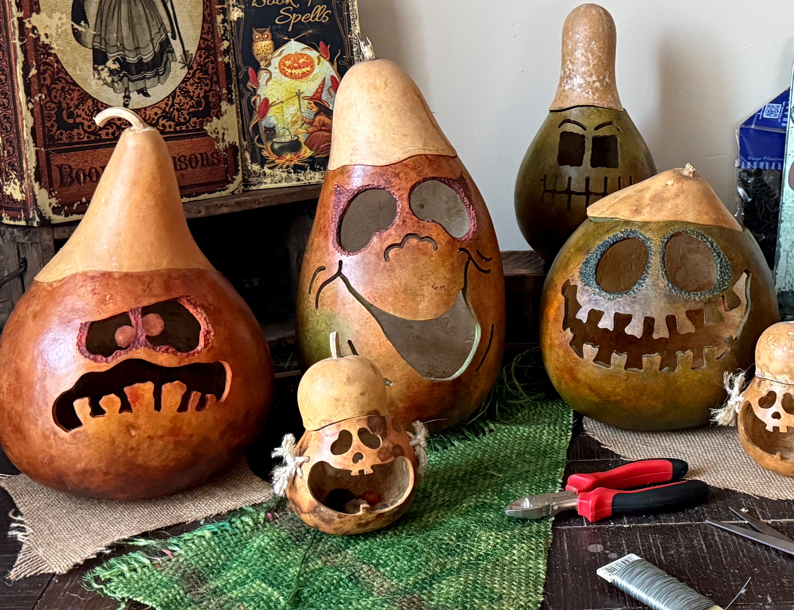 Decorative gourds with carved faces on a table with tools and books in the background.