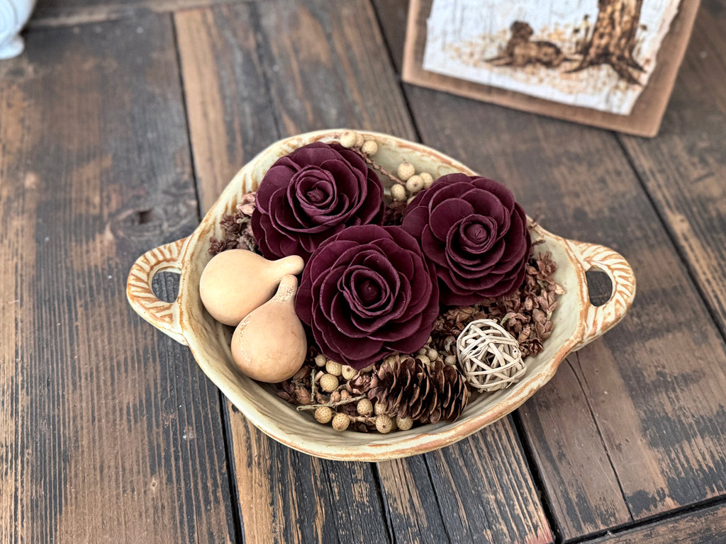 A small ceramic bowl filled with three wood flower blossoms and mini gourds. 