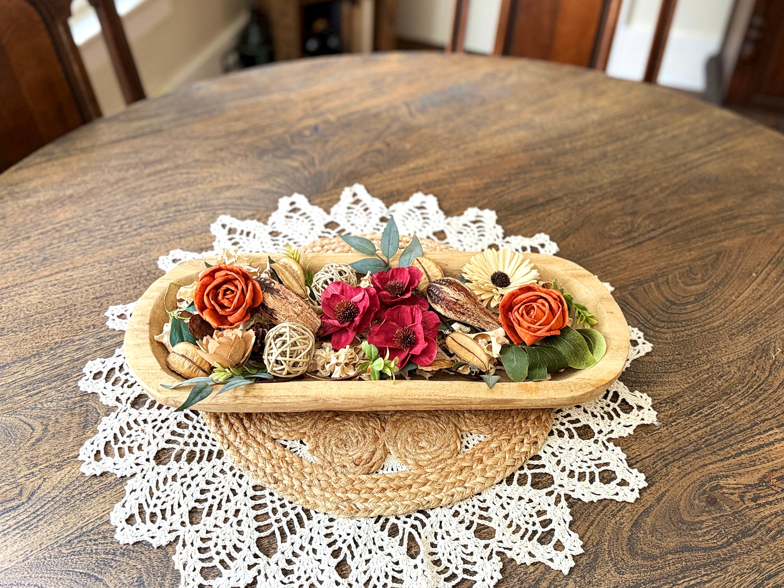 Decorative floral arrangement in a wood dough bowl on a dinning room table with a lace doily.