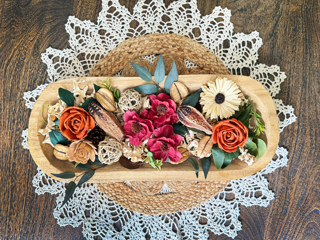 Decorative floral arrangement in a wood dough bowl on a dinning room table with a lace doily.