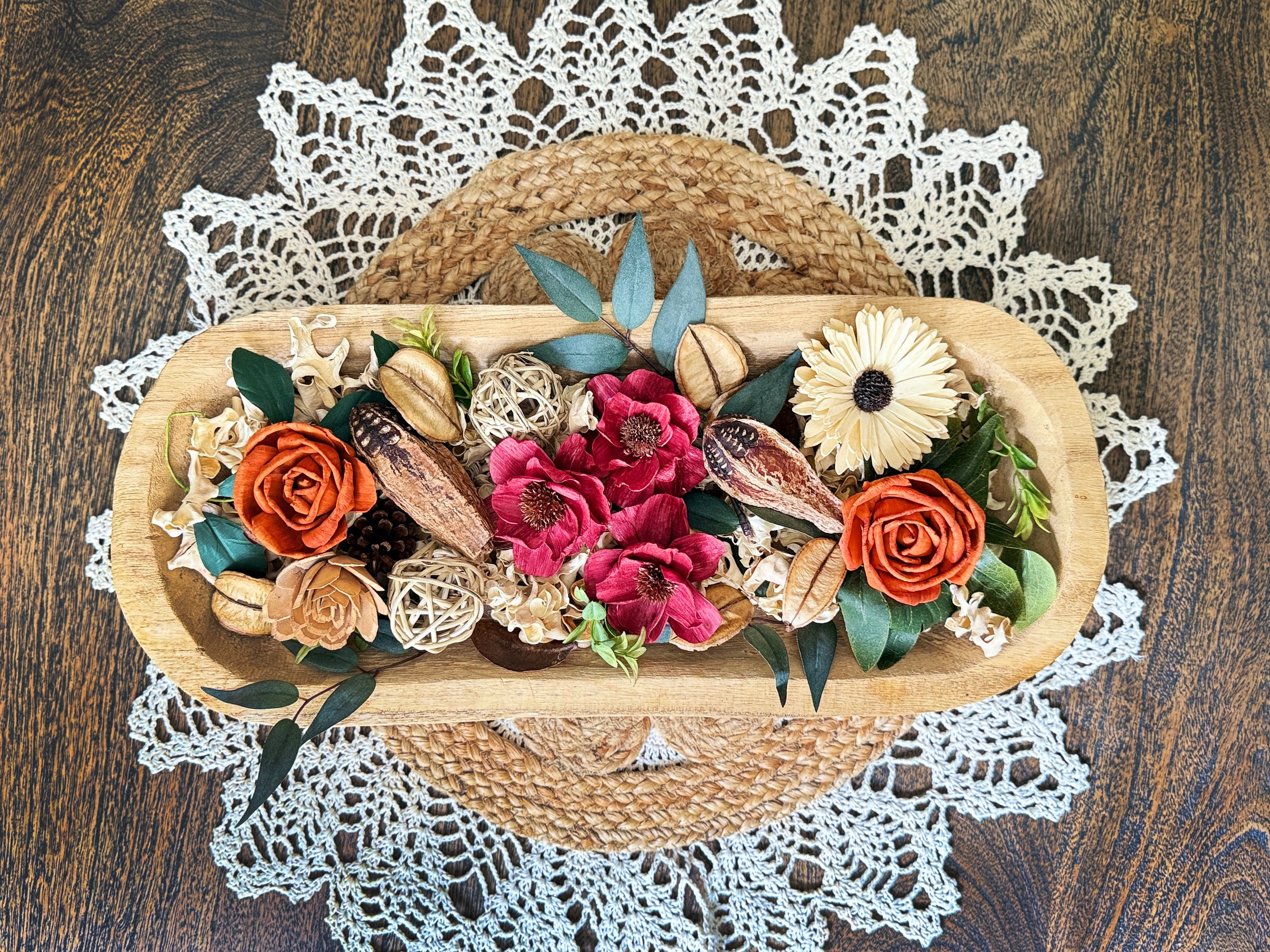 Decorative floral arrangement in a wood dough bowl on a dinning room table with a lace doily.