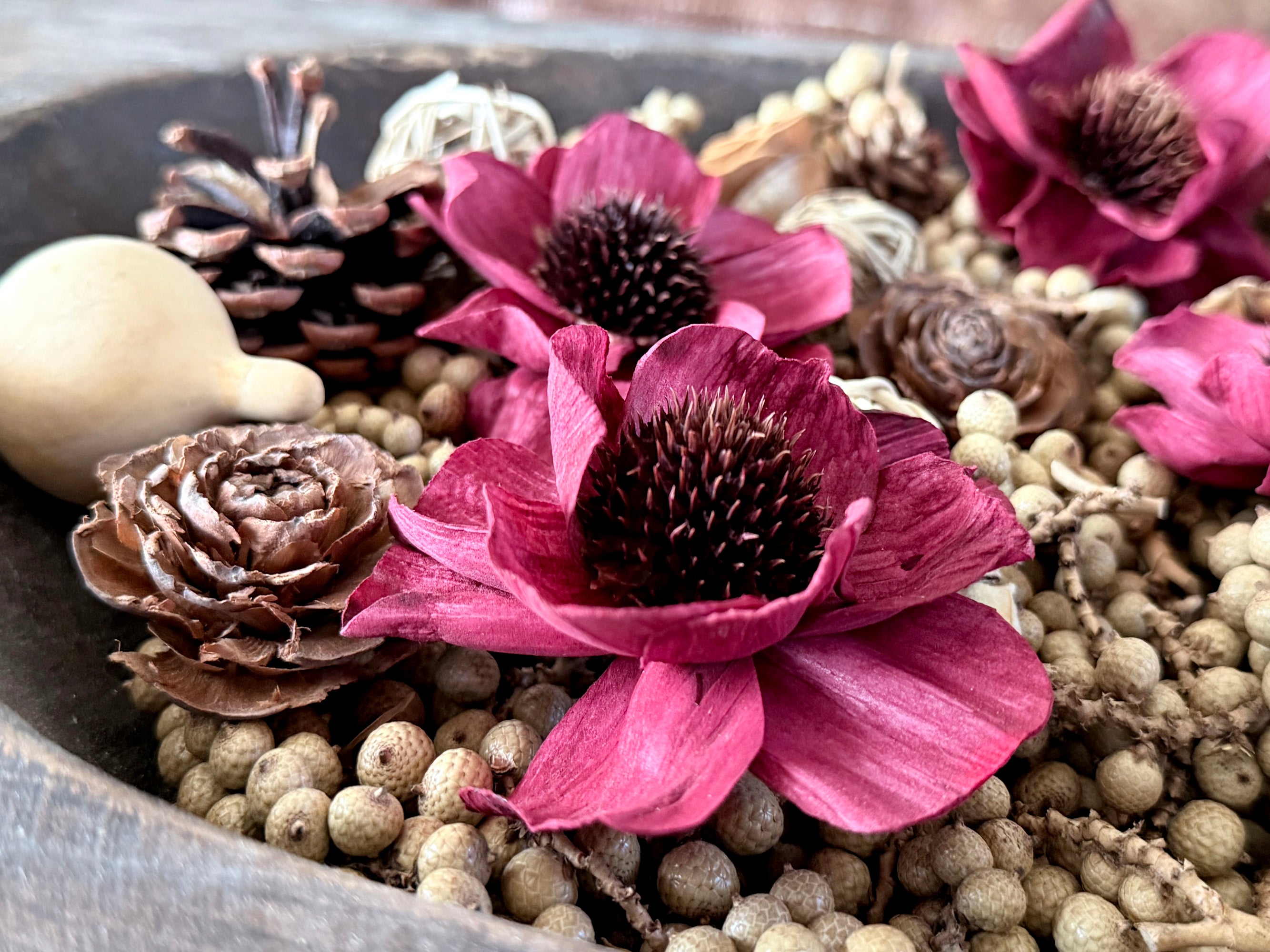Decorative arrangement with red flowers, pinecones, and berries in a bowl.
