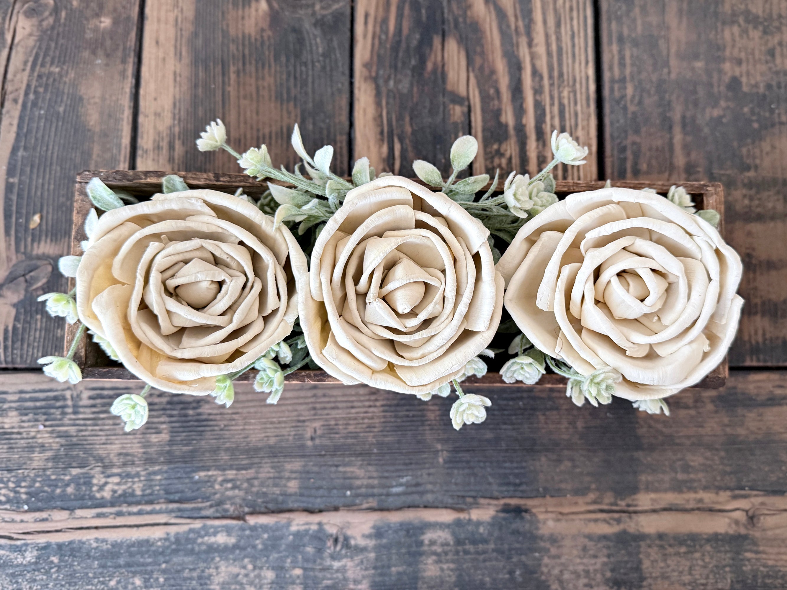 Three beige roses with green leaves on a wooden background
