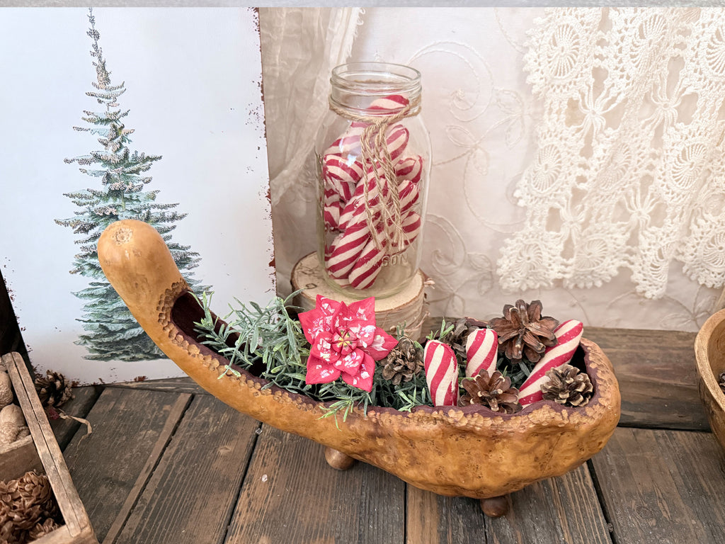 a hand carved gourd bowl holding arrangement of rosemary poinsettia wood flower blossoms and fabric candy canes