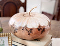 Artisan gourd vessel sitting on a stack of vintage books. The bottom half of the gourd is a neutral beige and the top has a fitted lid painted like a daisy. 