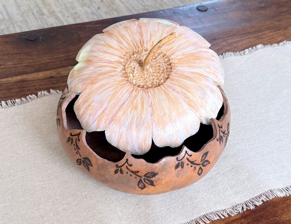 Decorative gourd bowl sitting on a coffee table with the flower blossom lid sitting ajar. 